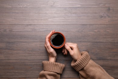 Photo of Woman with cup of coffee at wooden table, top view. Space for text