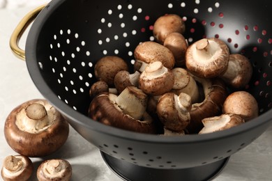 Raw mushrooms in black colander on table, closeup