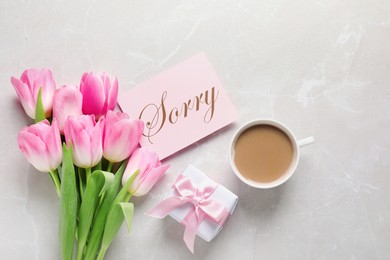 Card with word Sorry, cup of coffee, gift box and bouquet of tulips on light grey marble table, flat lay