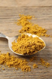 Photo of Spoon with dry curry powder on wooden table, closeup