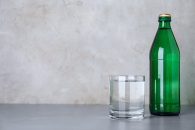 Photo of Glass and bottle with water on table against grey background, space for text