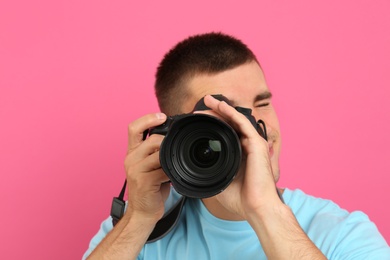 Photo of Young professional photographer taking picture on pink background