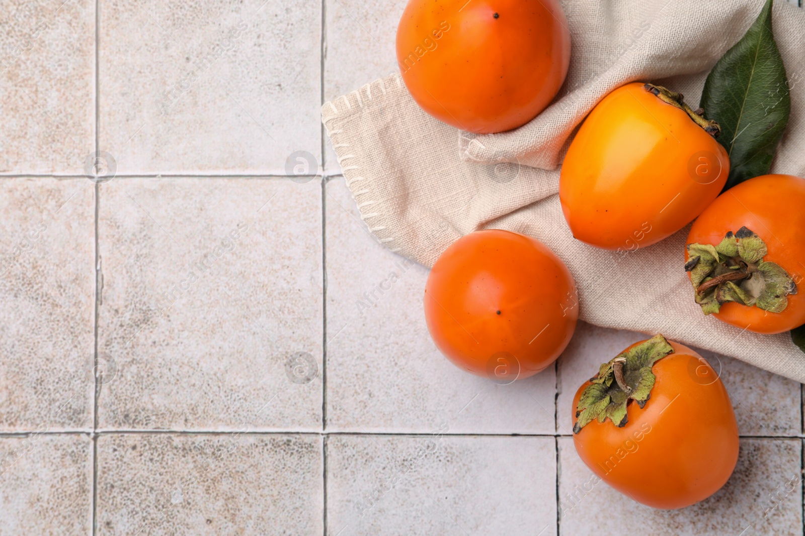 Photo of Delicious ripe juicy persimmons on tiled surface, flat lay. Space for text