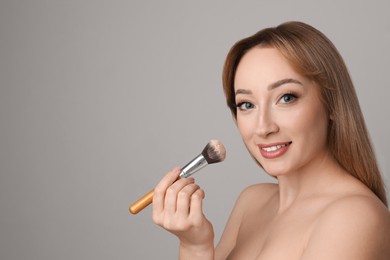 Photo of Beautiful young woman applying face powder with brush on grey background. Space for text