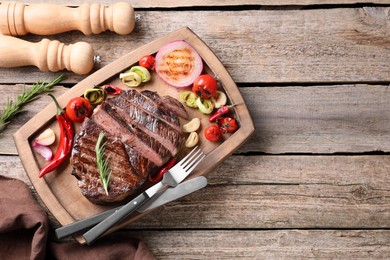 Delicious fried beef meat served with vegetables on wooden table, flat lay. Space for text