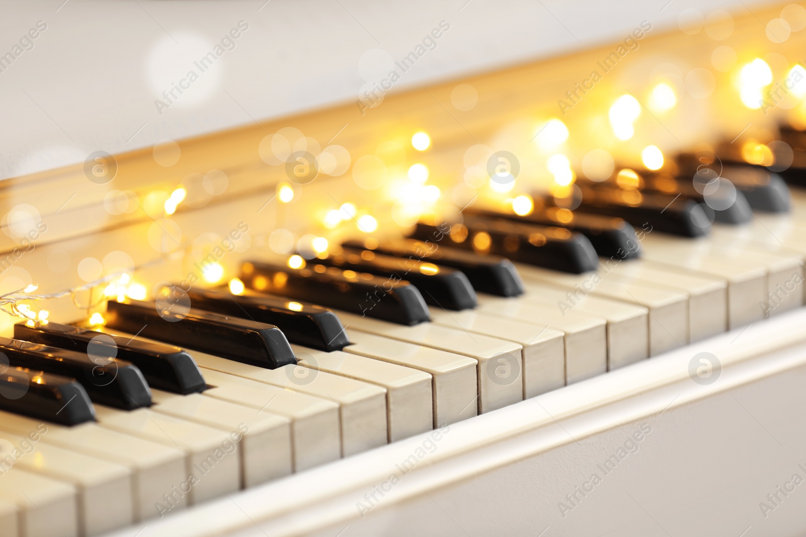 Photo of Glowing fairy lights on piano keys, closeup. Christmas music