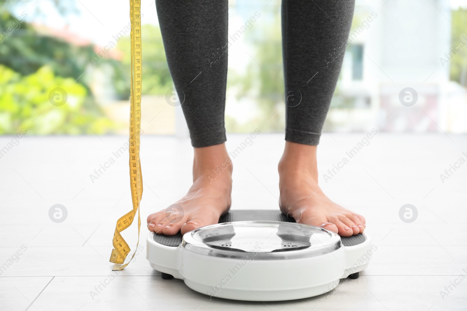 Photo of Woman with tape standing on scales indoors. Overweight problem