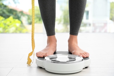 Photo of Woman with tape standing on scales indoors. Overweight problem