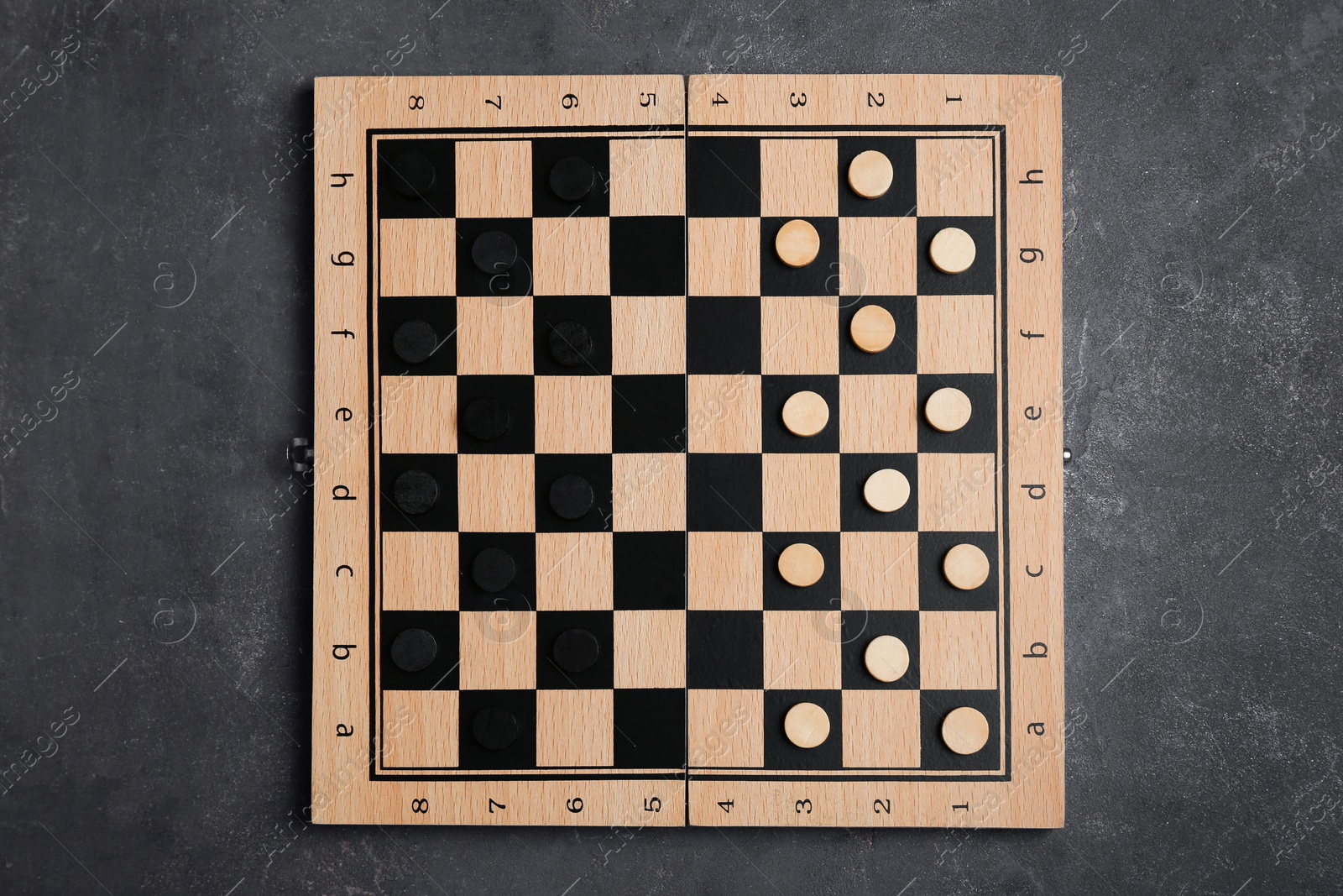 Photo of Wooden checkerboard with game pieces on grey table, top view