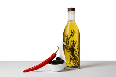 Bottle of cooking oil with rosemary, olives and chili pepper on white background