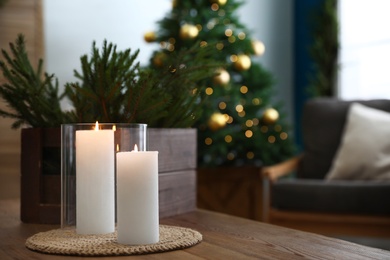 Photo of Burning candles and fir branches on wooden table in room decorated for Christmas