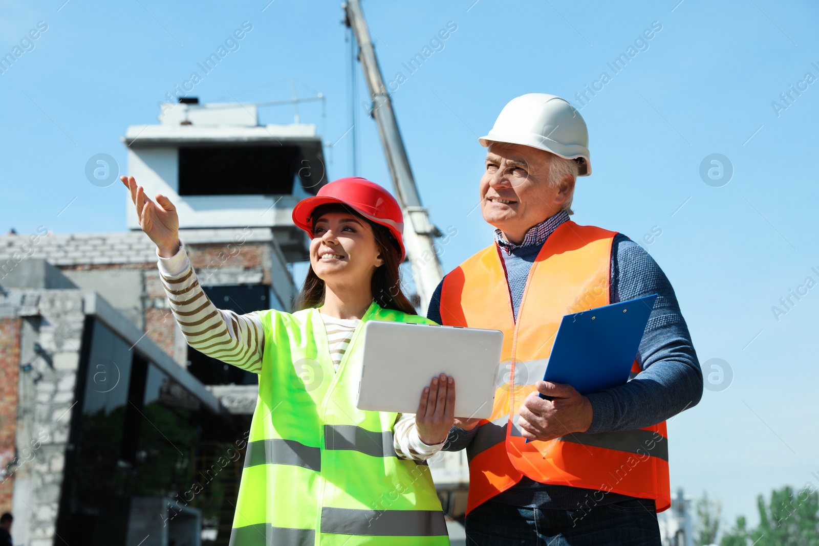 Photo of Professional engineer and foreman in safety equipment with tablet at construction site