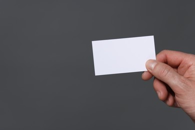 Man holding blank business card on grey background, closeup. Space for text