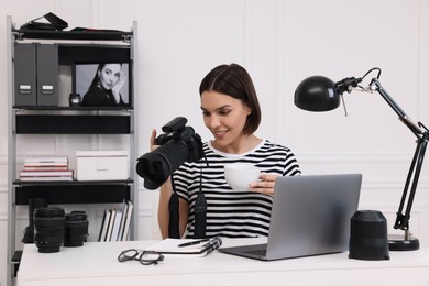 Young professional photographer with camera at table in modern photo studio