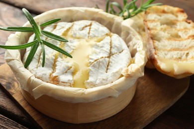 Photo of Tasty baked brie cheese, bread and rosemary on wooden board, closeup