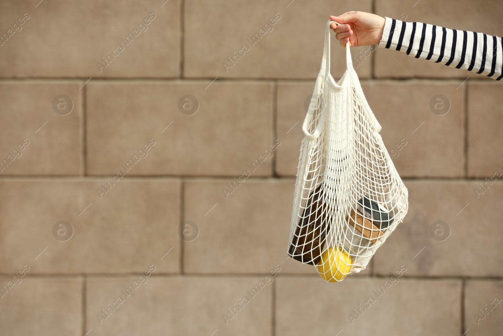 Photo of Conscious consumption. Woman with net bag of eco friendly products near stone wall, closeup. Space for text