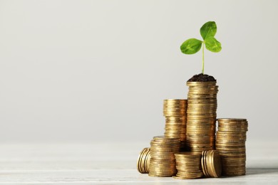 Photo of Stacked coins and green sprout on white wooden table, space for text. Investment concept