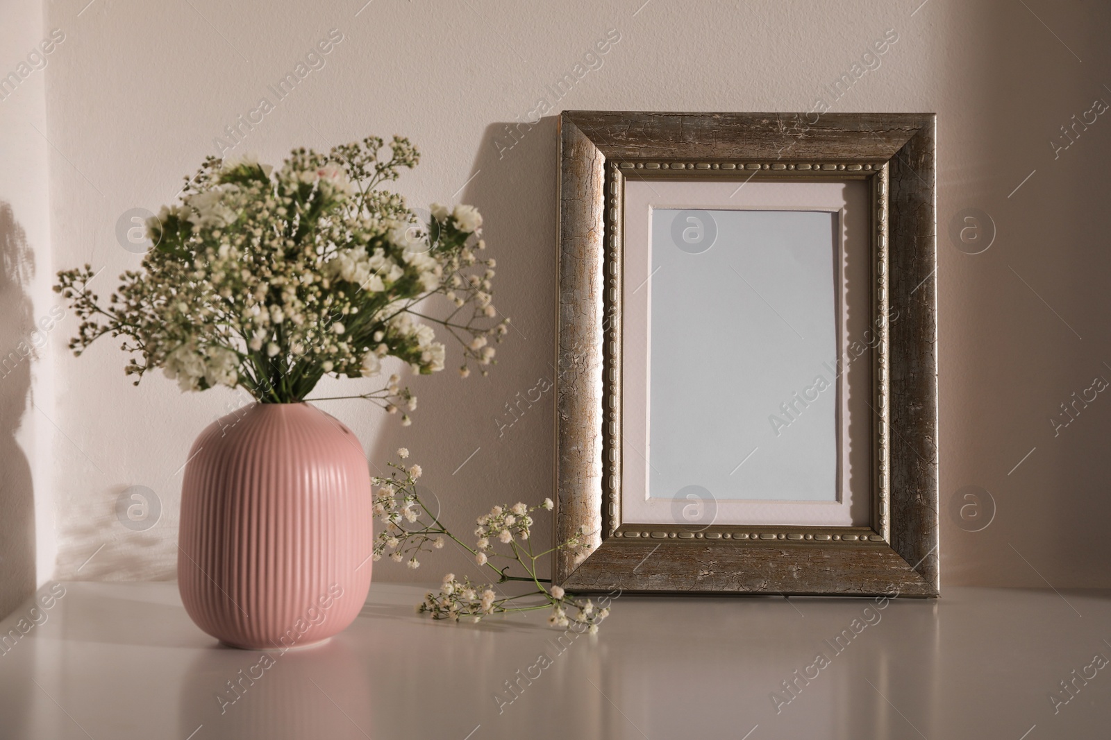 Photo of Empty photo frame and vase with flowers on table indoors