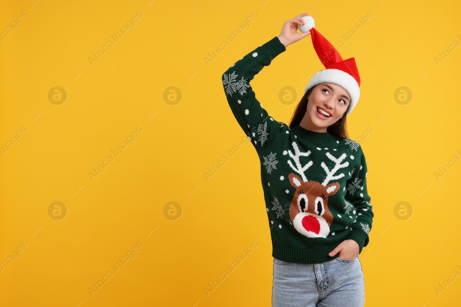Photo of Happy young woman in Christmas sweater and Santa hat on orange background. Space for text