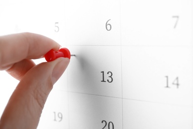 Photo of Woman pinning Friday 13th on calendar, closeup. Bad luck superstition