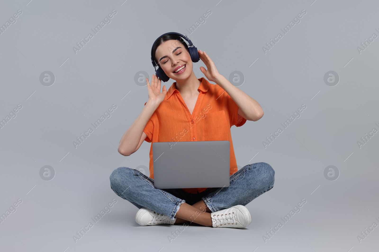 Photo of Happy woman with laptop listening to music in headphones on light gray background