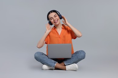 Happy woman with laptop listening to music in headphones on light gray background