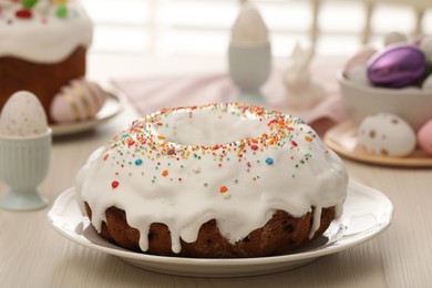 Delicious Easter cake decorated with sprinkles near painted eggs on white wooden table, closeup