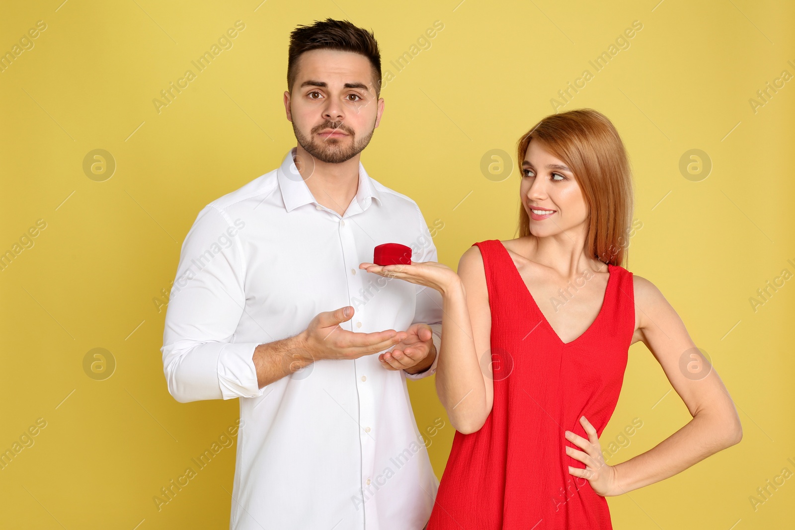 Photo of Young woman with engagement ring making proposal of marriage to her boyfriend on yellow background