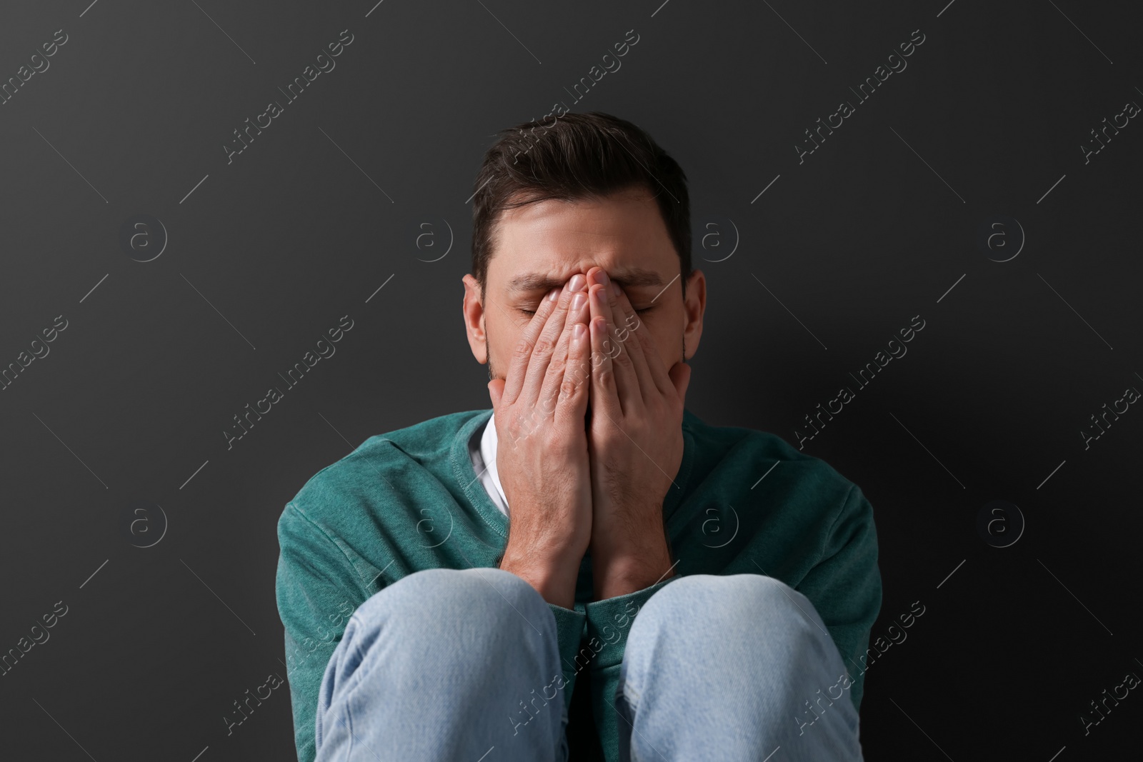 Photo of Upset mature man sitting near black wall