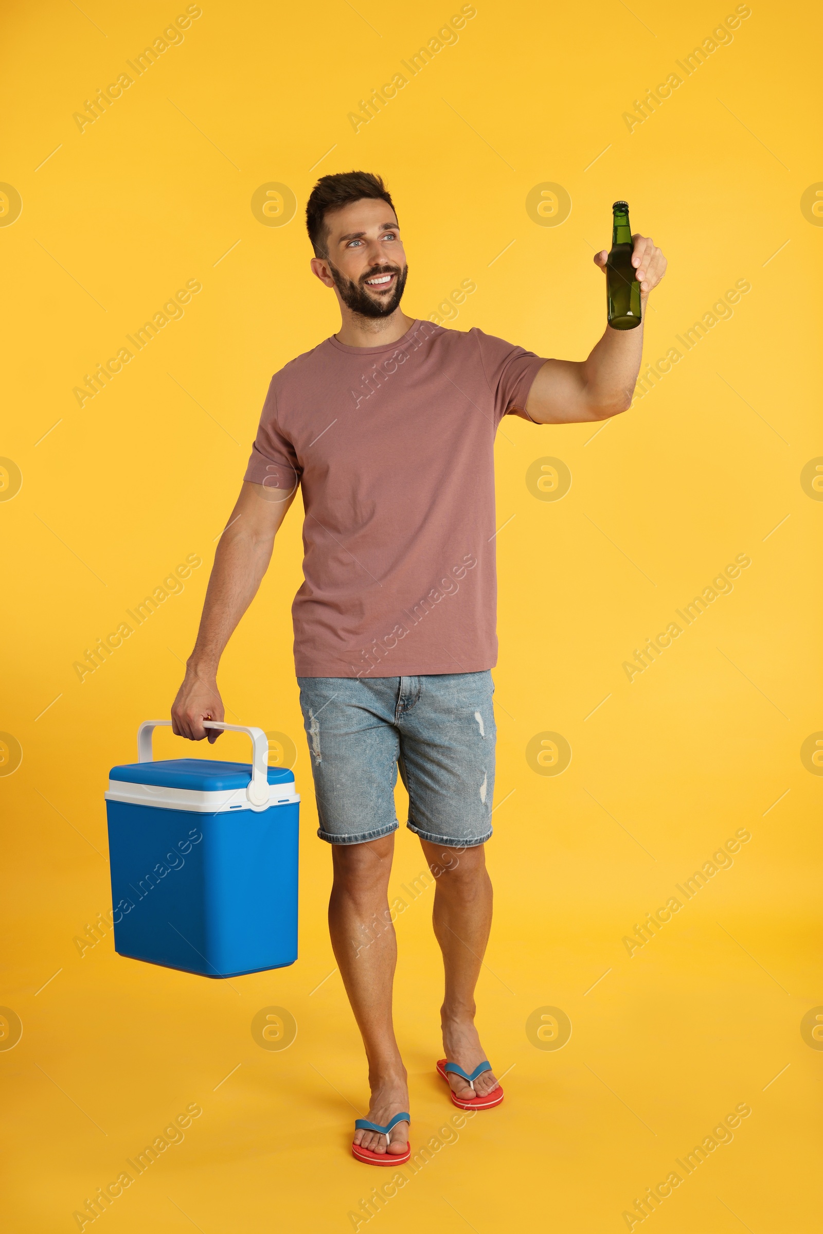 Photo of Happy man with cool box and bottle of beer on yellow background