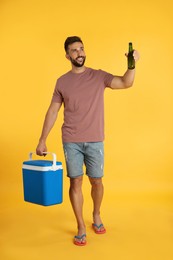 Photo of Happy man with cool box and bottle of beer on yellow background