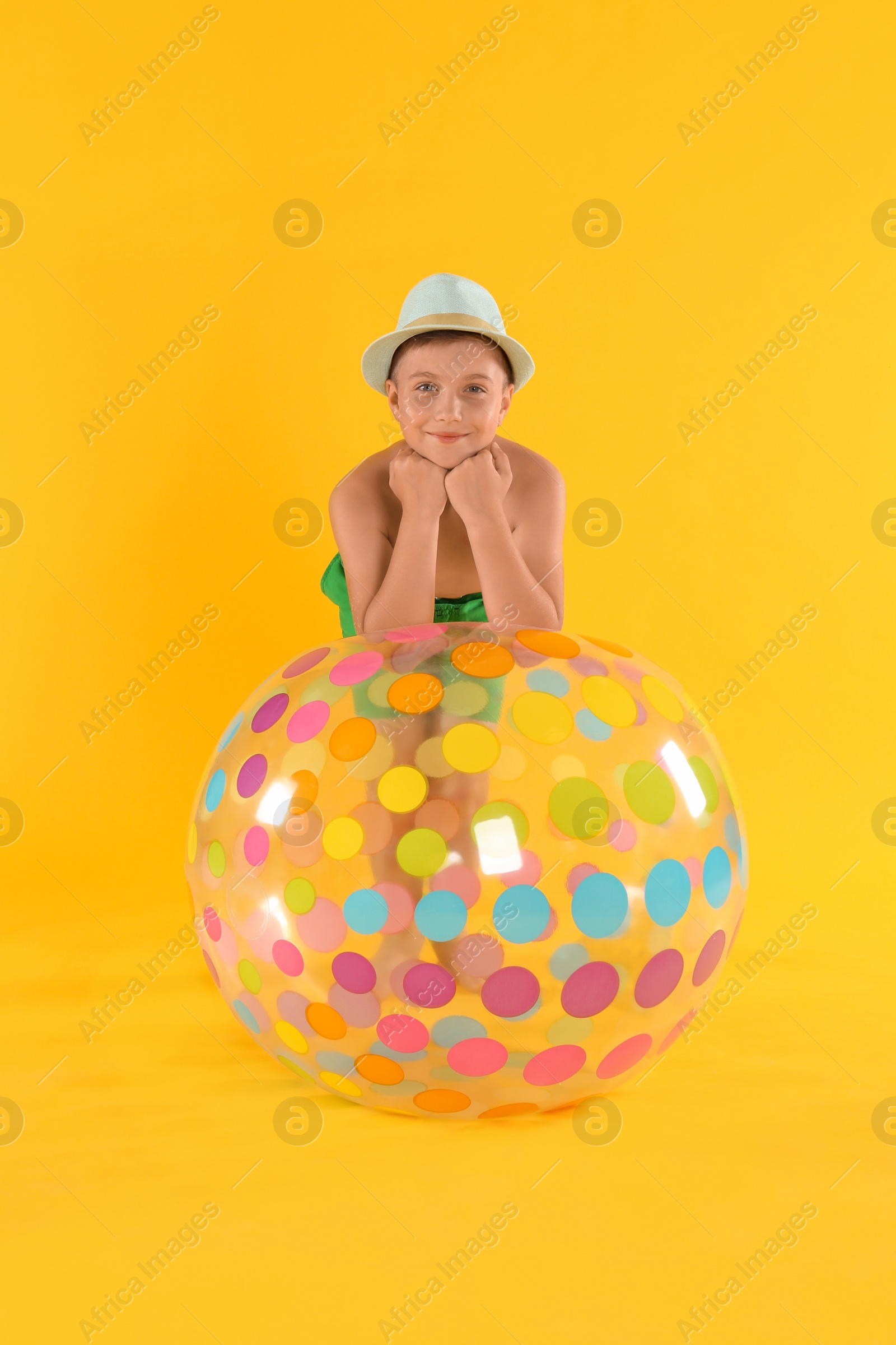 Photo of Cute little child in beachwear with bright inflatable ball on yellow background