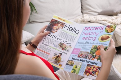Photo of Young woman reading cooking magazine at home, closeup