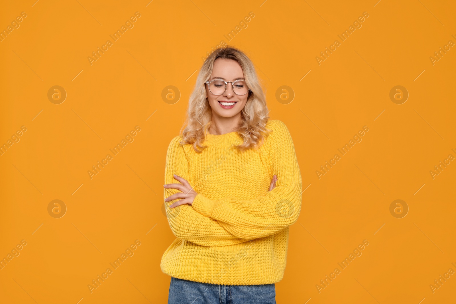 Photo of Happy woman in stylish warm sweater and eyeglasses on orange background
