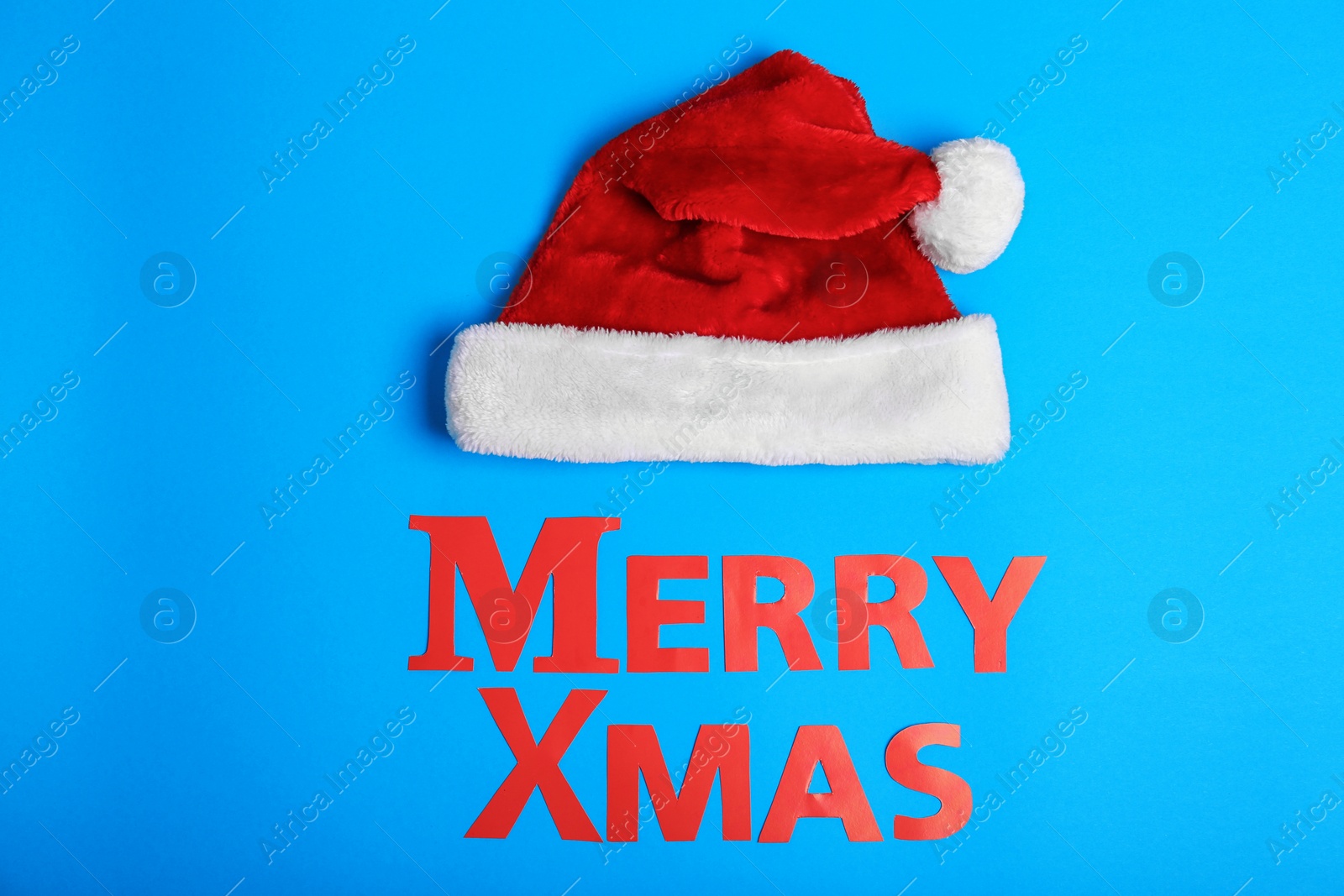 Photo of Santa Claus red hat and Merry Xmas made of paper letters on color background, top view