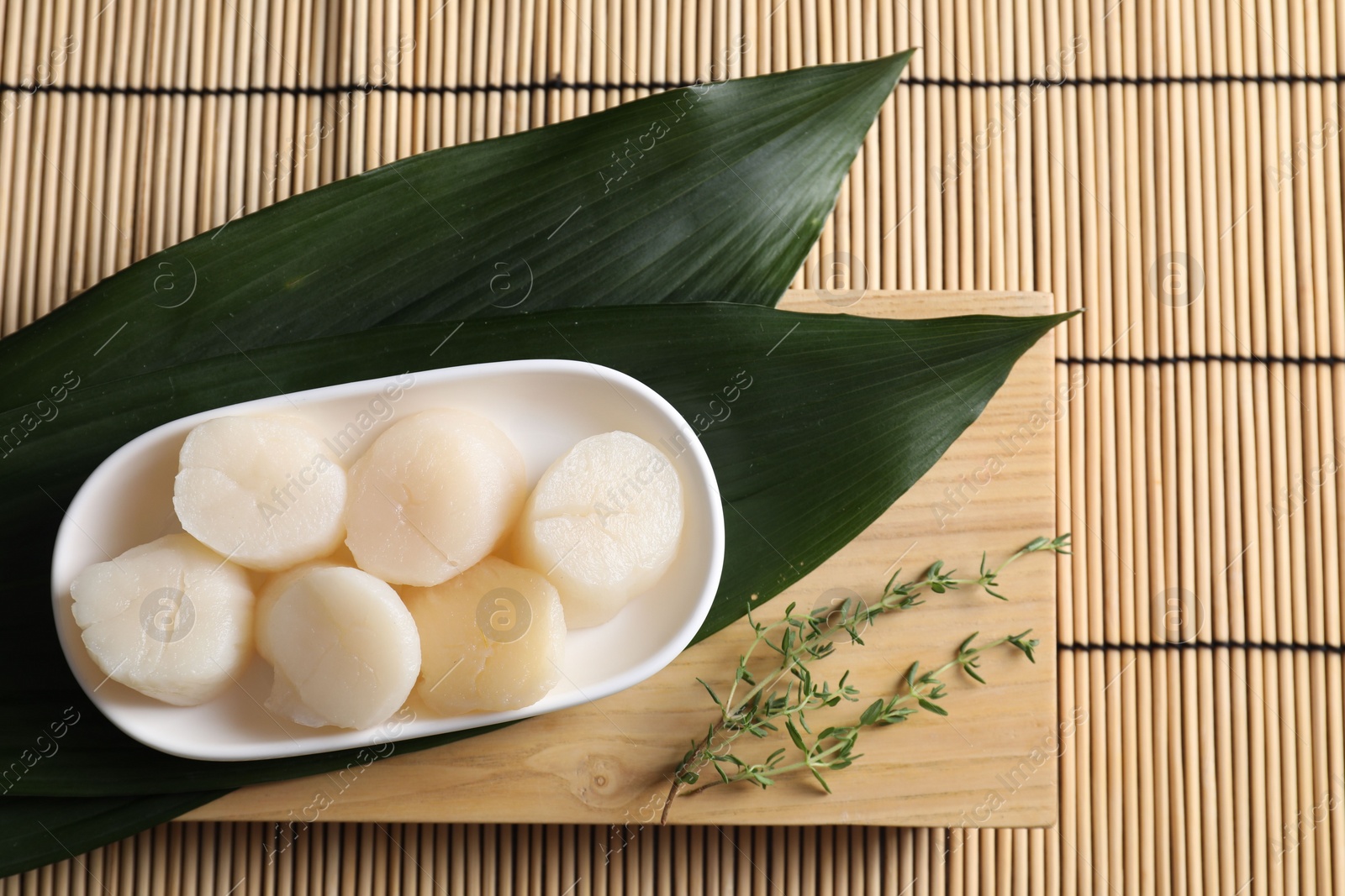 Photo of Fresh raw scallops, thyme and leaves on bamboo mat, flat lay