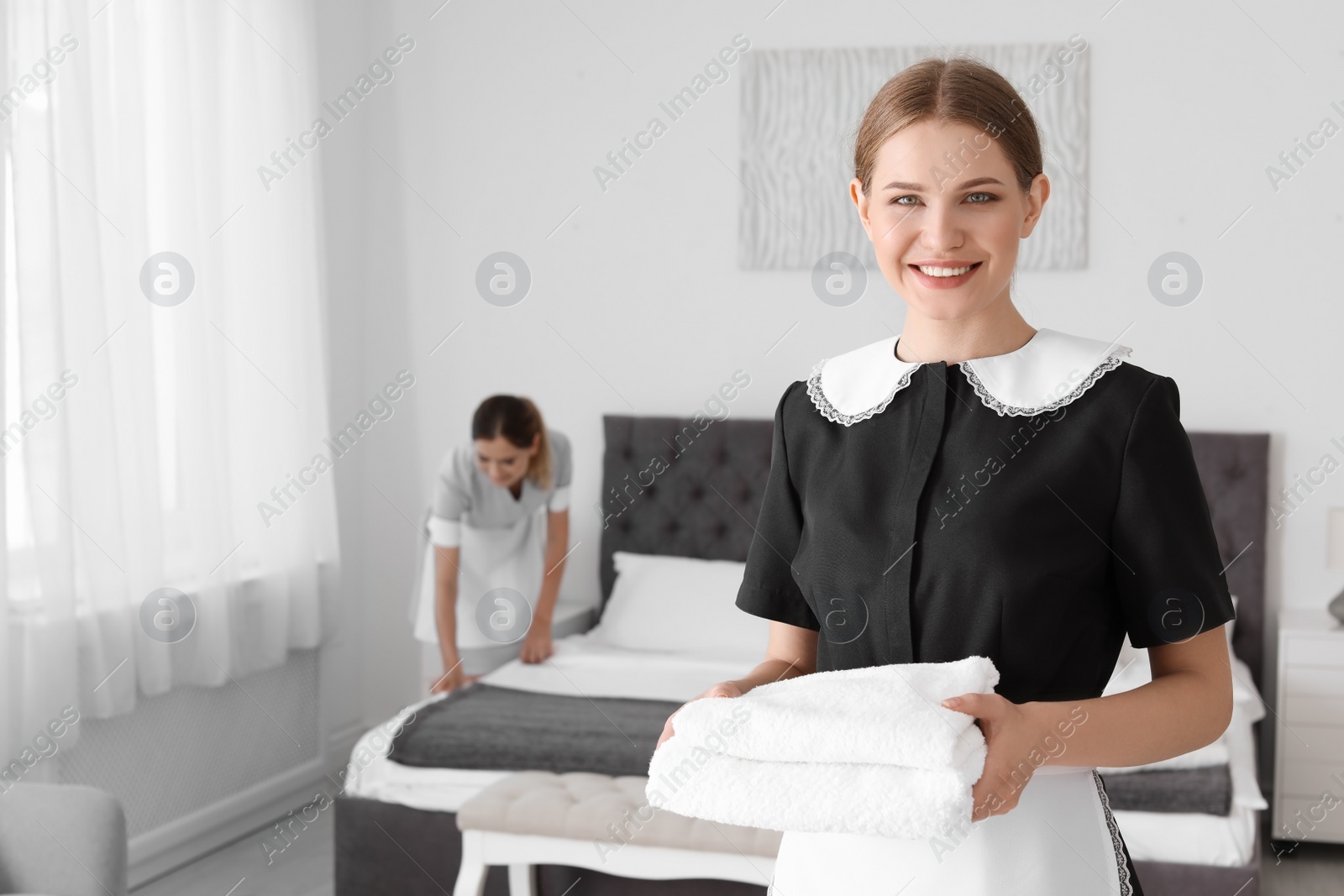 Photo of Young chambermaid holding pile of clean towels in bedroom