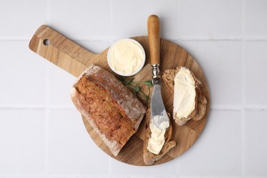 Tasty bread with butter and knife on white tiled table, top view