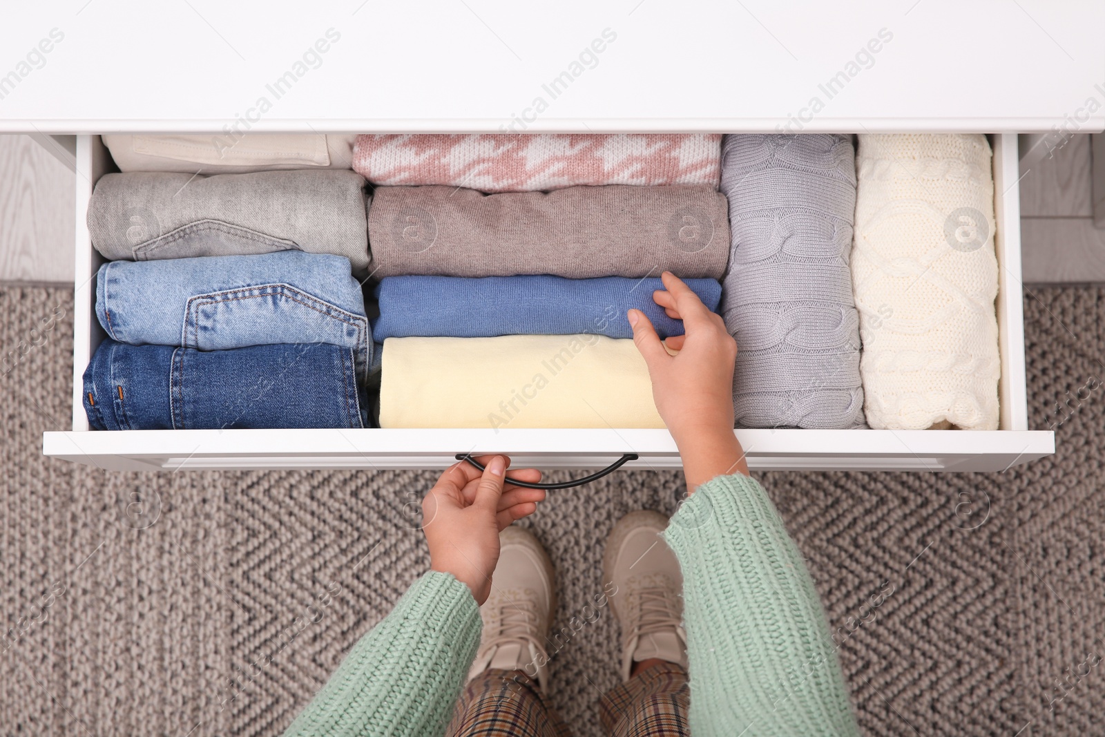 Photo of Woman opening drawer with folded clothes indoors, top view. Vertical storage