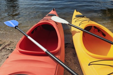 Photo of Modern kayaks with paddles on beach near river, closeup. Summer camp activity
