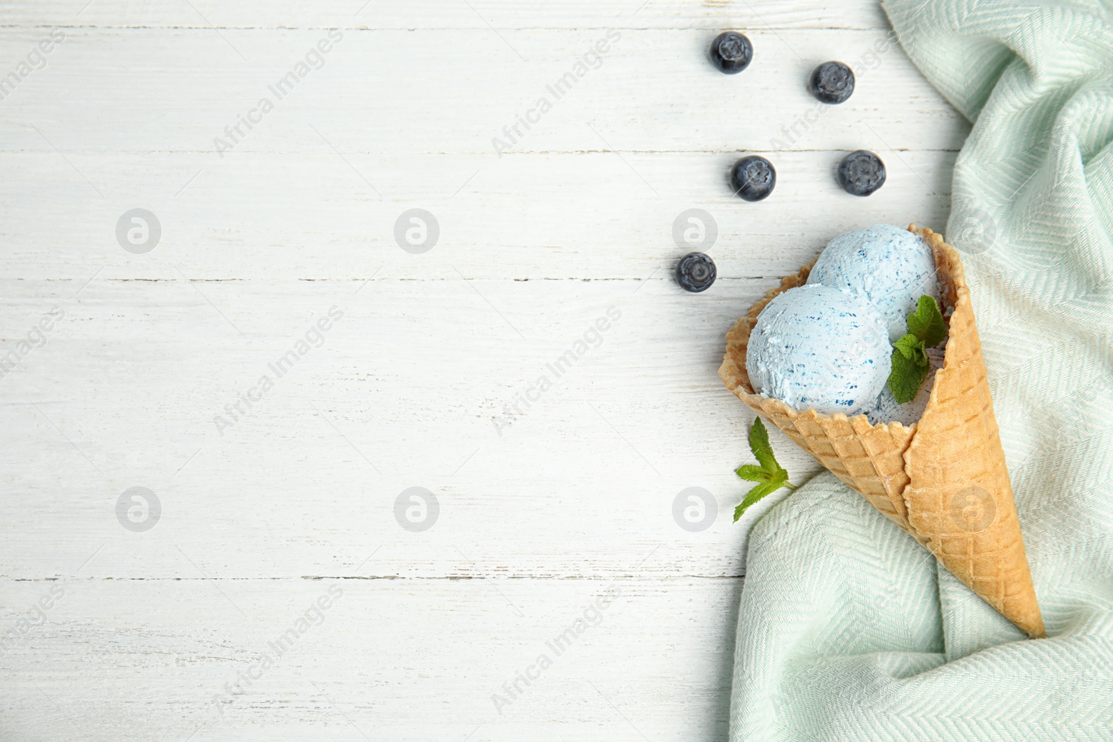 Photo of Flat lay composition with delicious ice cream in waffle cone on wooden table, space for text