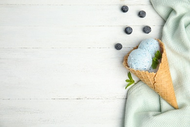 Photo of Flat lay composition with delicious ice cream in waffle cone on wooden table, space for text