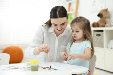 Photo of Mother and her little daughter painting with watercolor at home