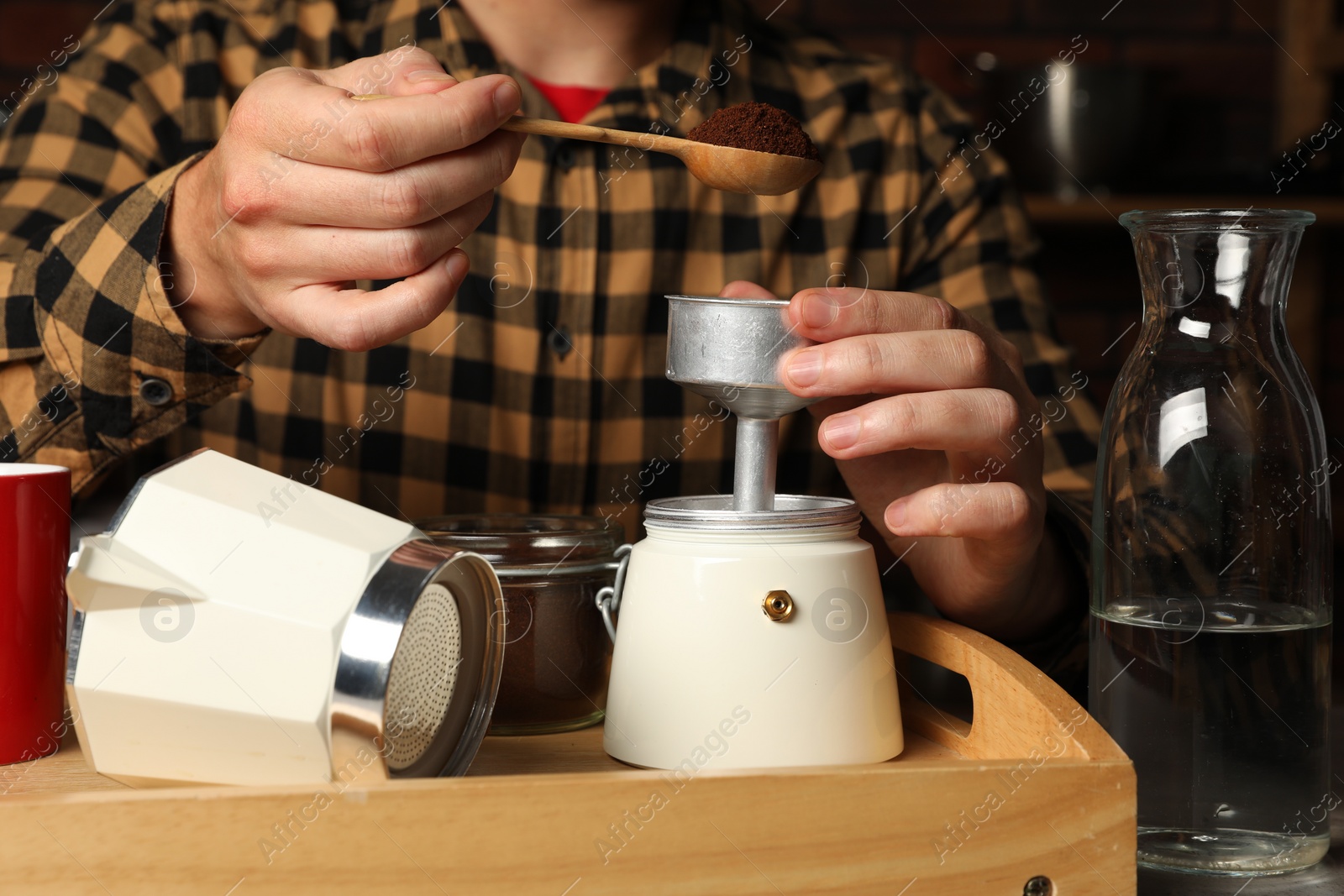 Photo of Man putting ground coffee into moka pot at table indoors, closeup