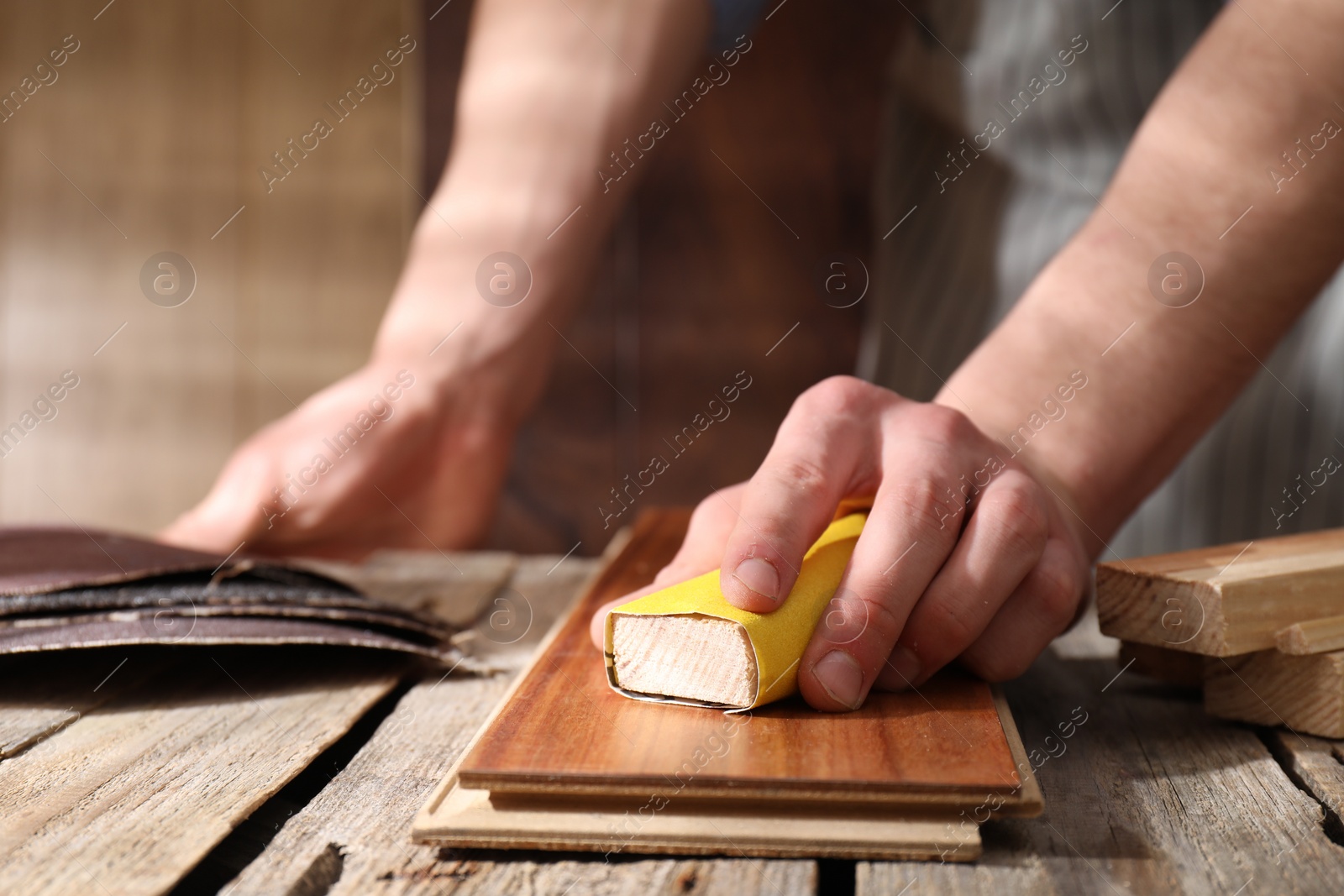 Photo of Man polishing wooden plank with sandpaper at table indoors, closeup