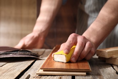 Man polishing wooden plank with sandpaper at table indoors, closeup