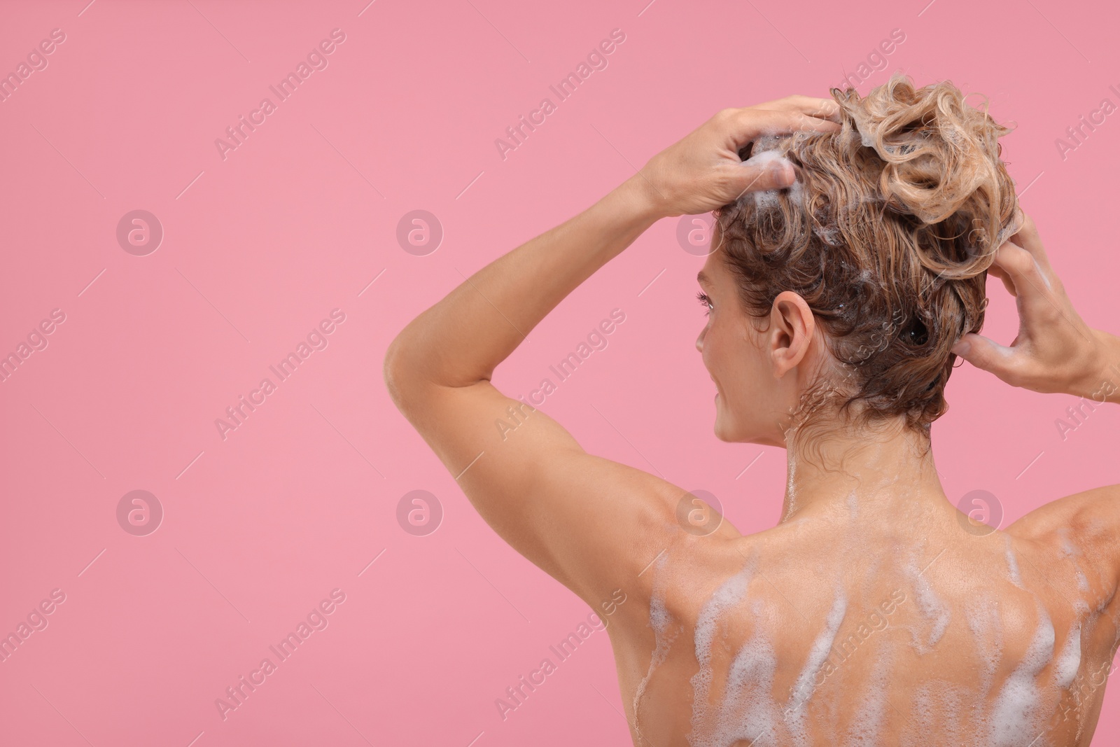 Photo of Woman washing hair on pink background, back view. Space for text