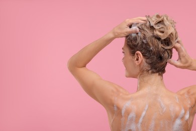 Photo of Woman washing hair on pink background, back view. Space for text