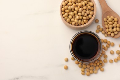 Photo of Soy sauce in bowl and soybeans on white table, flat lay. Space for text
