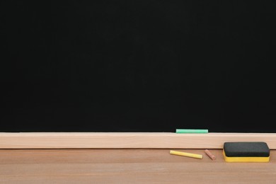 Colorful chalks and duster on wooden table near black board. Space for text